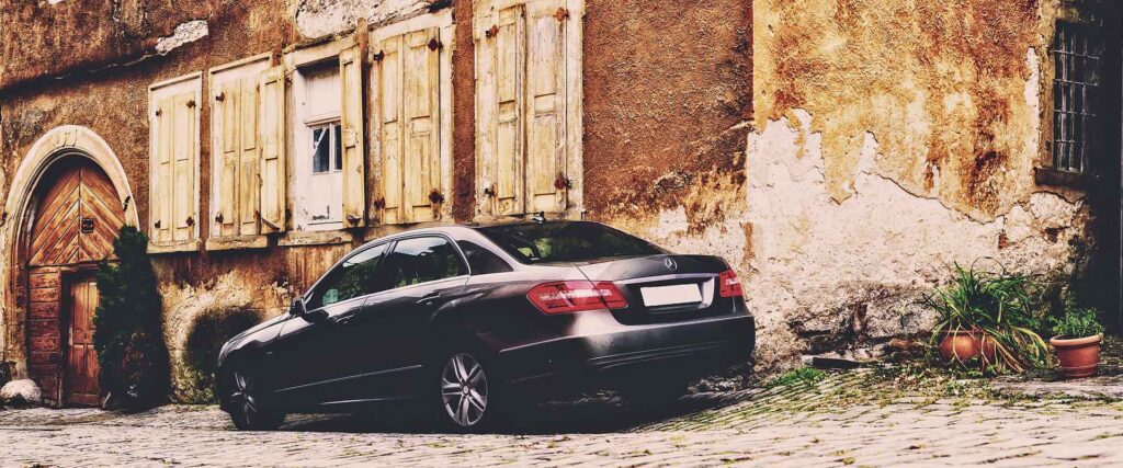 Old building and luxury sedan representing the Italian legal concept of scorpions - individuals who acquire what appears to be abandoned property adverse possession.